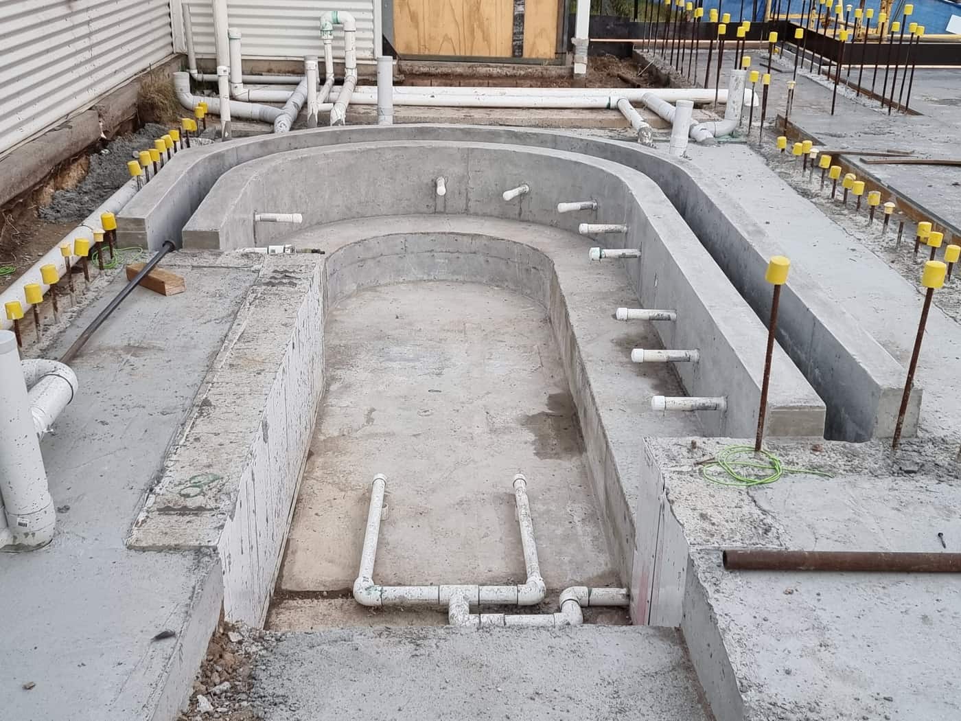 A curved concrete shell with the forms stripped, pipework set through the walls and starter bars capped along the top